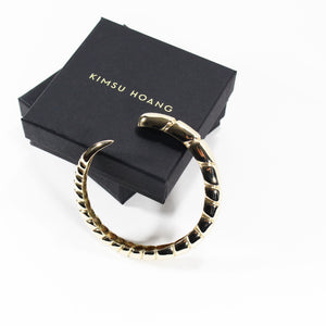 Gold bracelet with ridged texture next to stacked branded, black jewelry boxes.