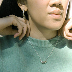 Model wearing silver earrings and small silver crescent pendant on chain necklace.