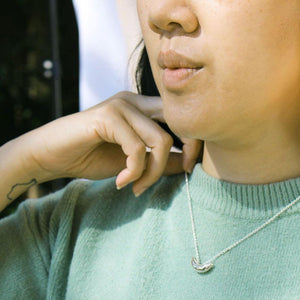 Side view of model wearing silver chain necklace with small crescent pendant.