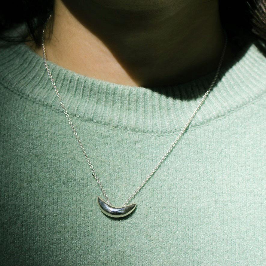 Front view of model wearing silver necklace with crescent pendant.