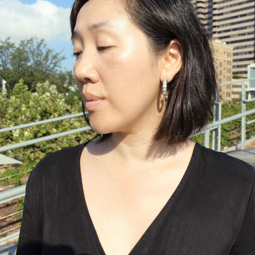 Front view of model wearing silver earring with ridged texture.