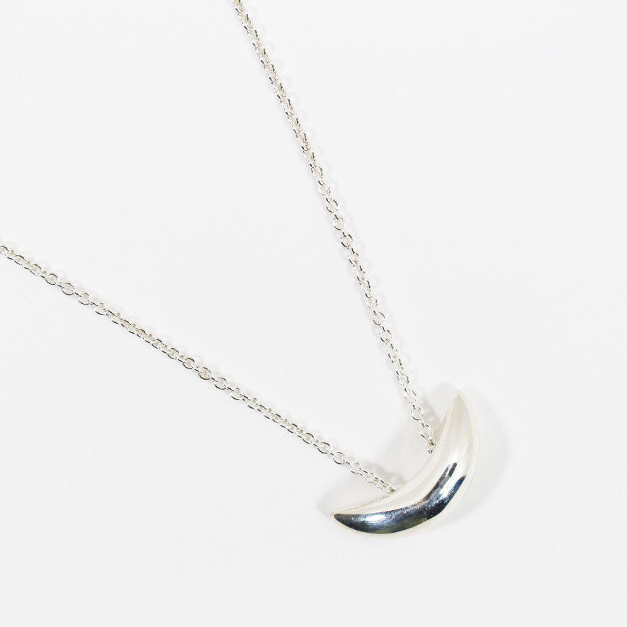 Close up view of small silver crescent shaped pendant on delicate chain necklace.
