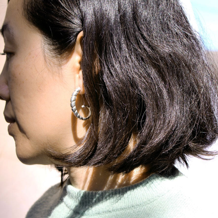 Side view of model wearing silver earring with ridged texture.