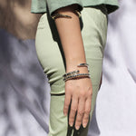 Model wearing one gold and two silver bracelets stacked on one wrist.