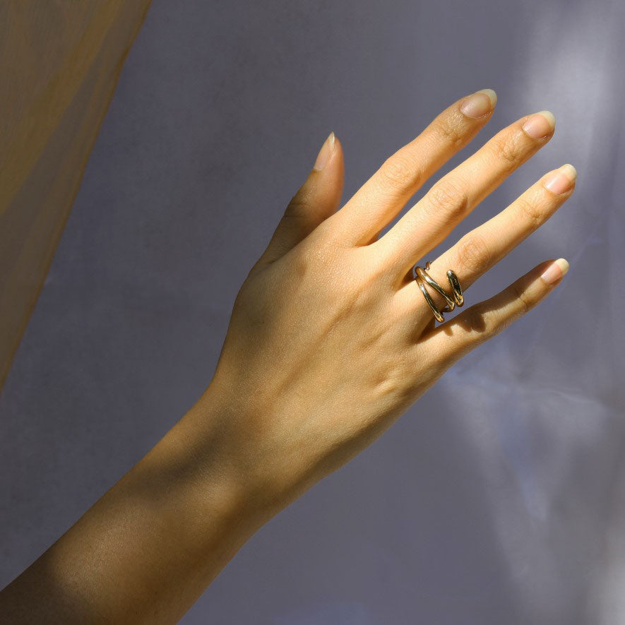 Model wearing two delicate, gold brass rings stacked on ring finger.