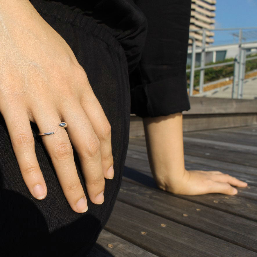 Model wearing delicate silver ring on ring finger.